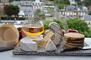 Cow cheeses of Normandy - camembert, livarot, neufchatel, pont l`eveque and glass of apple cider drink with houses of Etretat