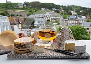 Cow cheeses of Normandy - camembert, livarot, neufchatel, pont l`eveque and glass of apple cider drink with houses of Etretat