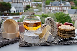 Cow cheeses of Normandy - camembert, livarot, neufchatel, pont l`eveque and glass of apple cider drink with houses of Etretat