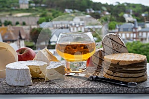 Cow cheeses of Normandy - camembert, livarot, neufchatel, pont l`eveque and glass of apple cider drink with houses of Etretat