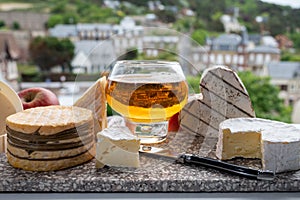 Cow cheeses of Normandy - camembert, livarot, neufchatel, pont l`eveque and glass of apple cider drink with houses of Etretat