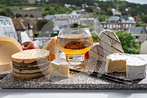 Cow cheeses of Normandy - camembert, livarot, neufchatel, pont l`eveque and glass of apple cider drink with houses of Etretat