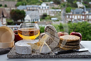 Cow cheeses of Normandy - camembert, livarot, neufchatel, pont l`eveque and glass of apple cider drink with houses of Etretat