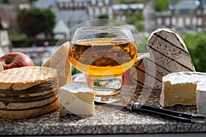 Cow cheeses of Normandy - camembert, livarot, neufchatel, pont l`eveque and glass of apple cider drink with houses of Etretat