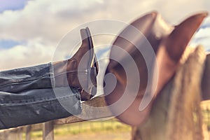 Cowboy boots and hat with feet up on fence resting with legs crossed