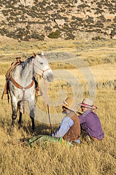 Cowboy and Cowgirl Sitting in Grass Holding Horse photo