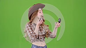 Cowboy girl is holding a brush and powdering her face. Green screen