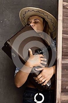 Cowboy girl or pretty woman in stylish hat and blue plaid shirt holding gun and old suitcase
