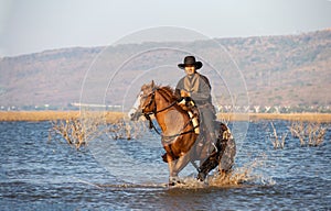 Cowboy on his horse walking through dust in the lake