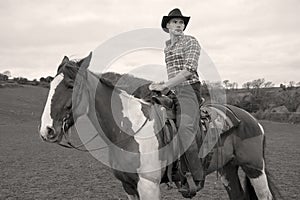 Cowboy on horseback, horse riding with chequered shirt, field, hill side and trees in background