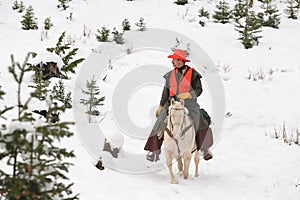 Cowboy hunter riding white horse in snow