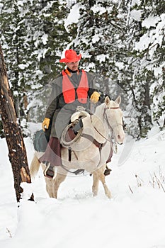 Cowboy hunter riding white horse in snow