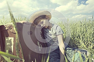 Young cowboy relaxes over his heavy suitcase in a meadow photo