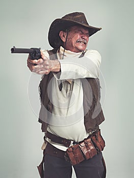 Cowboy, senior man and shooting gun, weapon or pistol in studio with costume isolated on a white background. Western