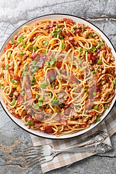 Cowboy Spaghetti with Ground beef, bacon, cheddar cheese, onion, pepper and tomatoes closeup on the plate. Vertical top view