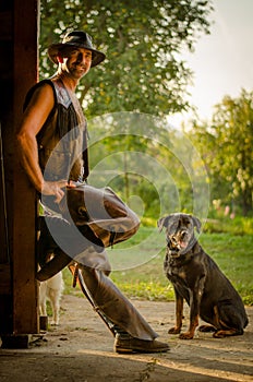 Cowboy stands with dog at the barn. A handsome man with a hat. A sympathetic man.