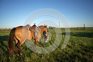 Cowboy walking with his horse across a ranch field