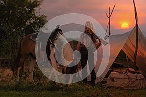 Cowboy woman lovingly caring for her gun and horse while at camp at sunset