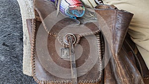 A cowboys saddle bag hanging on the back of his saddled horse.