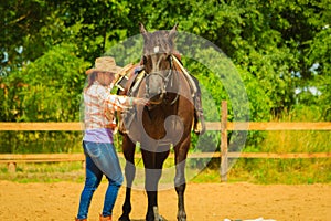 Cowgirl getting horse ready for ride on countryside