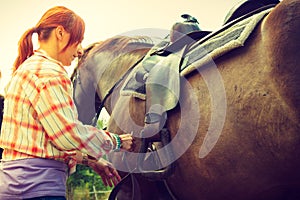 Cowgirl getting horse ready for ride on countryside