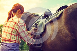 Cowgirl getting horse ready for ride on countryside