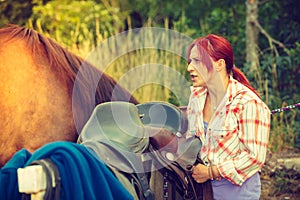 Cowgirl getting horse ready for ride on countryside