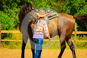 Cowgirl getting horse ready for ride on countryside