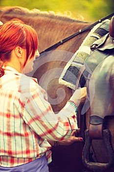 Cowgirl getting horse ready for ride on countryside