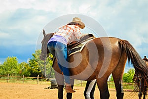 Cowgirl getting horse ready for ride on countryside