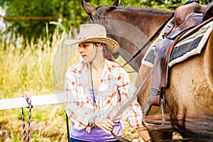 Cowgirl getting horse ready for ride on countryside