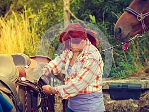 Cowgirl getting horse ready for ride on countryside