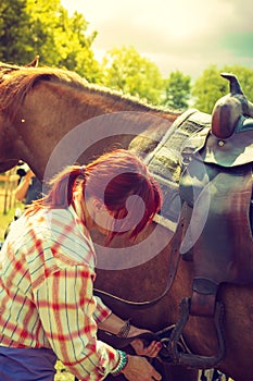 Cowgirl getting horse ready for ride on countryside