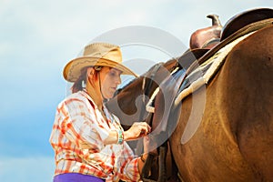 Cowgirl getting horse ready for ride on countryside