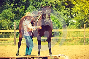 Cowgirl getting horse ready for ride on countryside