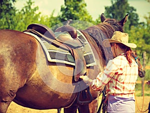 Cowgirl getting horse ready for ride on countryside