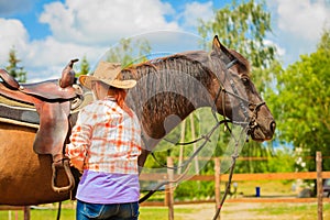 Cowgirl getting horse ready for ride on countryside