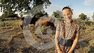 Cowgirl in glasses shies looks smiles cows graze on background overgrown asphalt evening sun hot summer in village