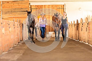 Cowgirl and jockey walking with horses in stable