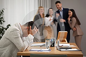 Coworkers bullying their colleague at workplace in office, space for text