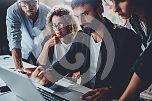 Coworkers working together in modern office.Bearded man talking with colleague and using laptop while sitting at the