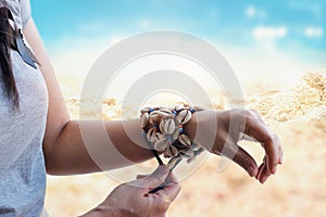 Cowrie shell bracelets on the wrist of woman on beach background