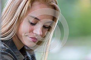 Coy blonde girl in a park with downcast gaze