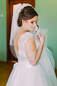 Coy bride in white dress posing, holding cute little boutenniere and looking over her shoulder