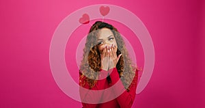 Coy and flirty young woman giggles at secret admirer, Valentines Day studio pink