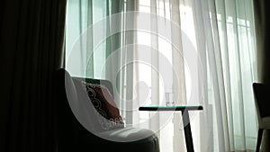 A cozy armchair and a table with a glass of water against the background of the Transparent curtain on the window