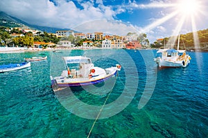 Cozy Assos village in Kefalonia. Colorful boats in azure bay under morning sunlight. Sommer vacation in Greece