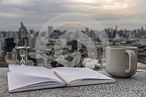 Cozy atmosphere with Evening coffee with a city view. There is a cup of coffee, hourglass, diaries, notebook, pencil to record