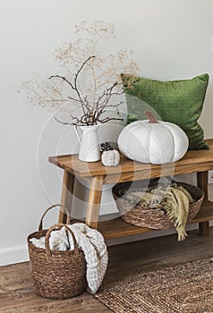 Cozy autumn interior - autumn decor on an oak bench in the living room, a basket with blankets, pillows. Minimalism style