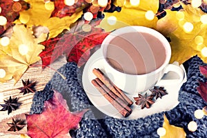 Cozy autumn morning with cup of cocoa with cinnamon, star anise, cozy sweater and autumn leaves on wooden background